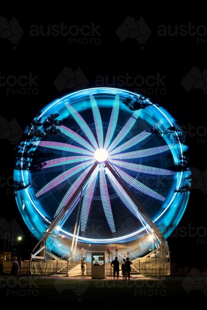 Ferris wheel at night with silhouetted people in foreground - Australian Stock Image