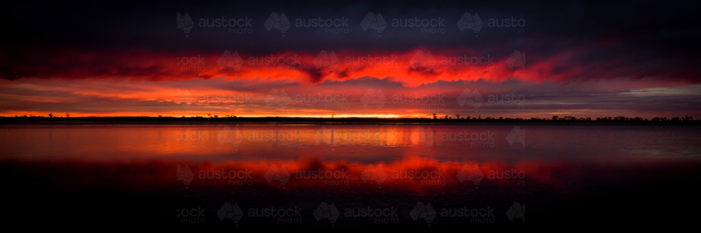 Fiery red sunrise glowing above calm lake waters - Australian Stock Image