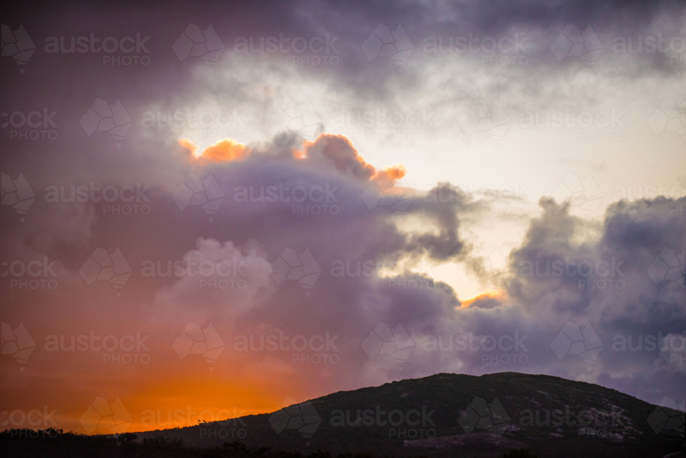 Fiery sunset clouds above a darkened hillside - Australian Stock Image