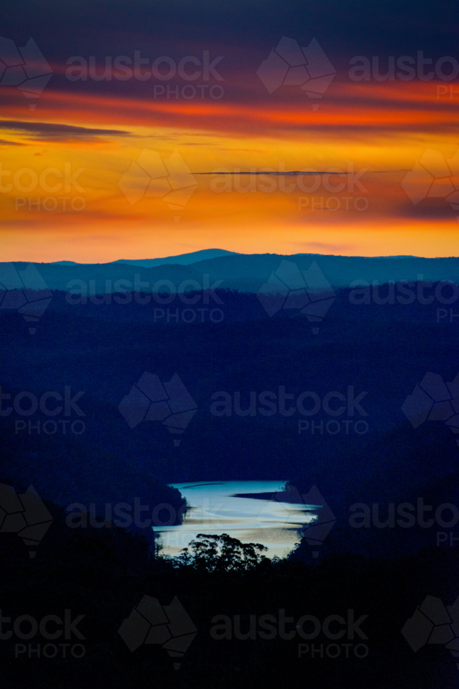 Fiery sunset over layered mountain ridges with a winding river glowing below. - Australian Stock Image
