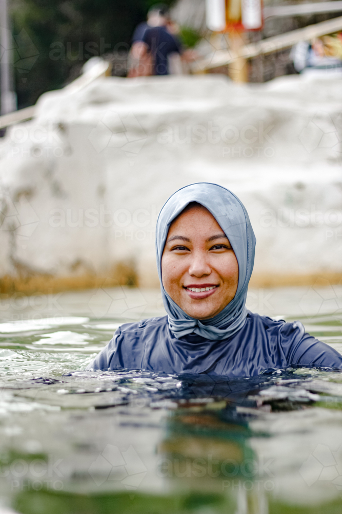 Filipina woman wearing light blue headscarf submerged in a clear tidal pool - Australian Stock Image