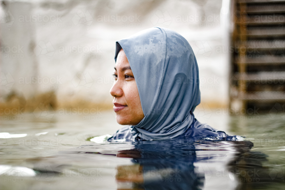 Filipina woman wearing light blue headscarf submerged in a clear tidal pool - Australian Stock Image