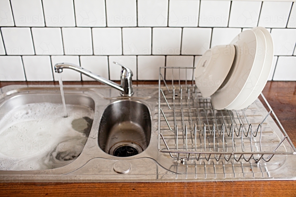 Filling the sink with washing up water to do the dishes - Australian Stock Image