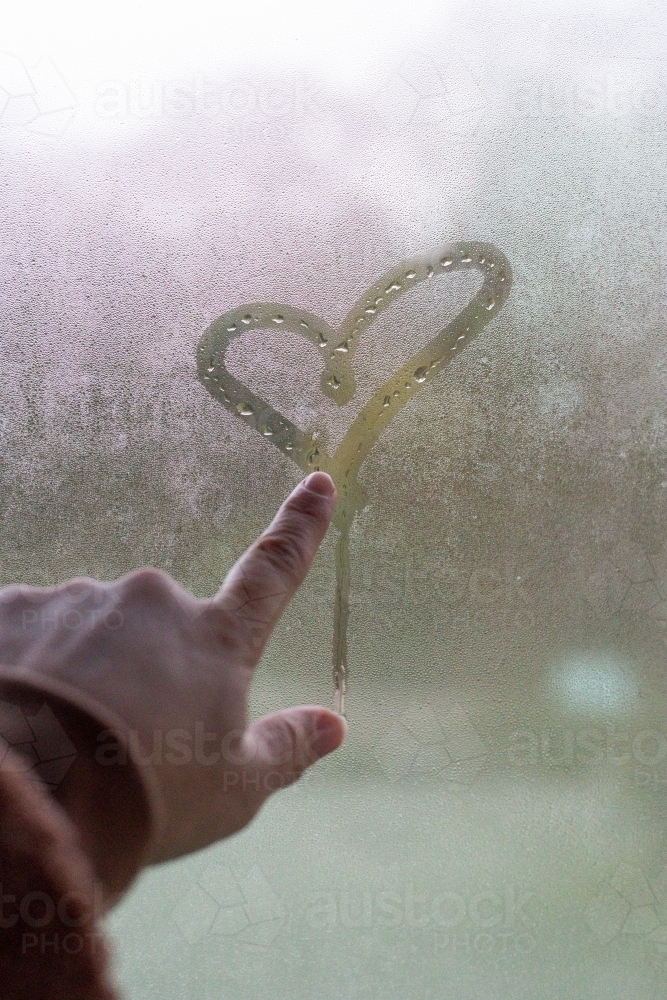 Finger drawing heart in condensation on winter window - Australian Stock Image