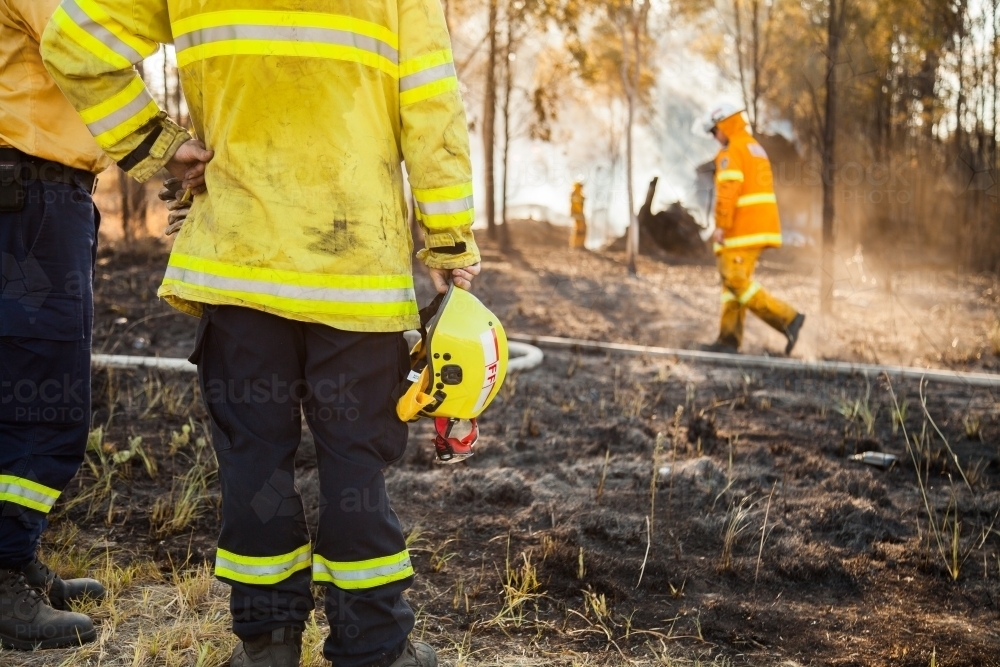 Fire fighter standing beside burnt grass holding safety helmet in hand - Australian Stock Image