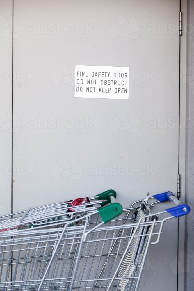 Fire safety door do not obstruct, do not keep open sign with trollies blocking door - Australian Stock Image