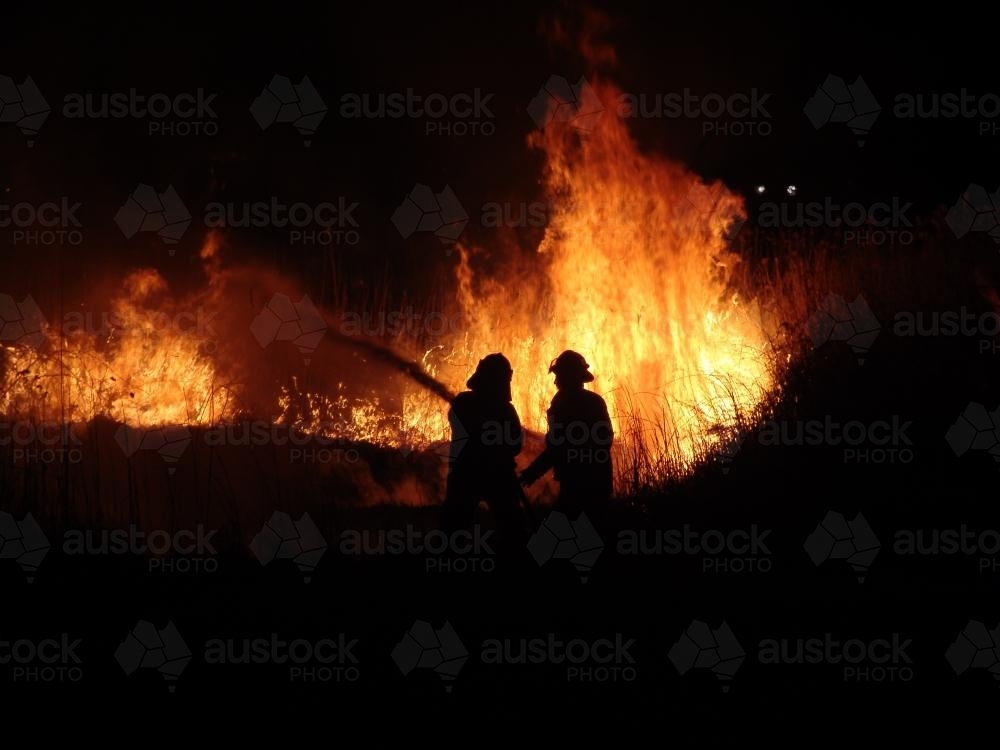 Firefighters fighting a grass fire at night silhouetted against the fire - Australian Stock Image