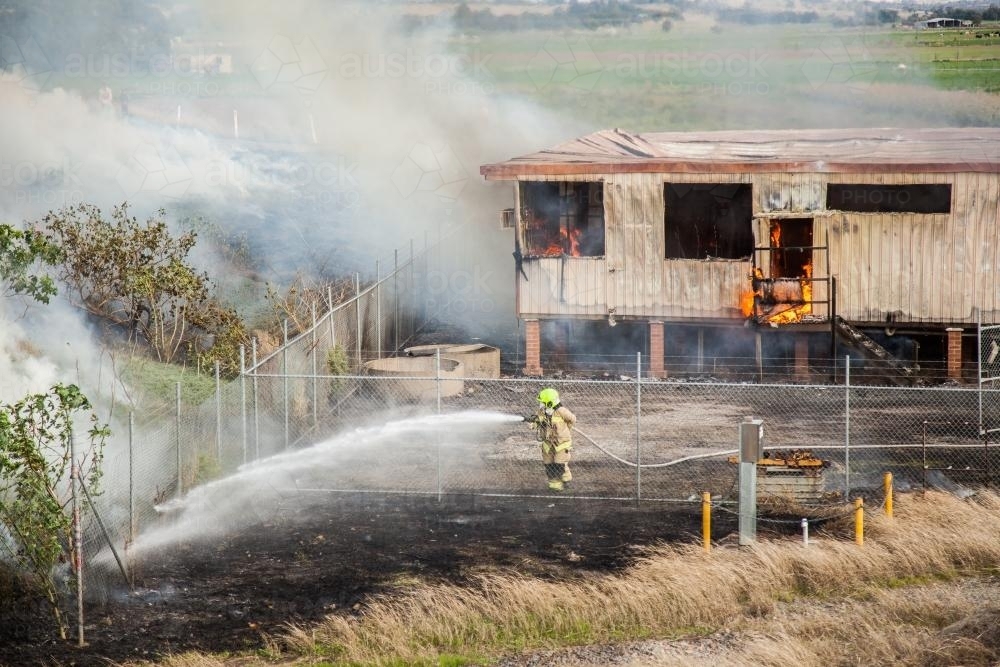 Firefighters putting out the flames of a burning shed and grass - Australian Stock Image