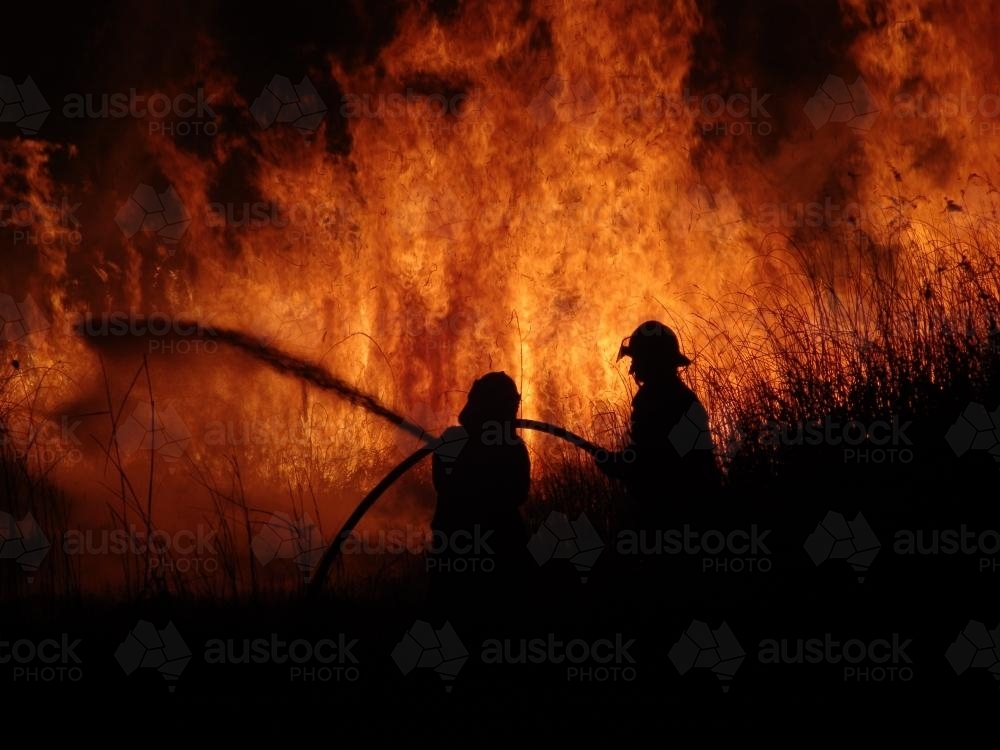 Firemen fighting a grass fire at night silhouetted against the fire - Australian Stock Image