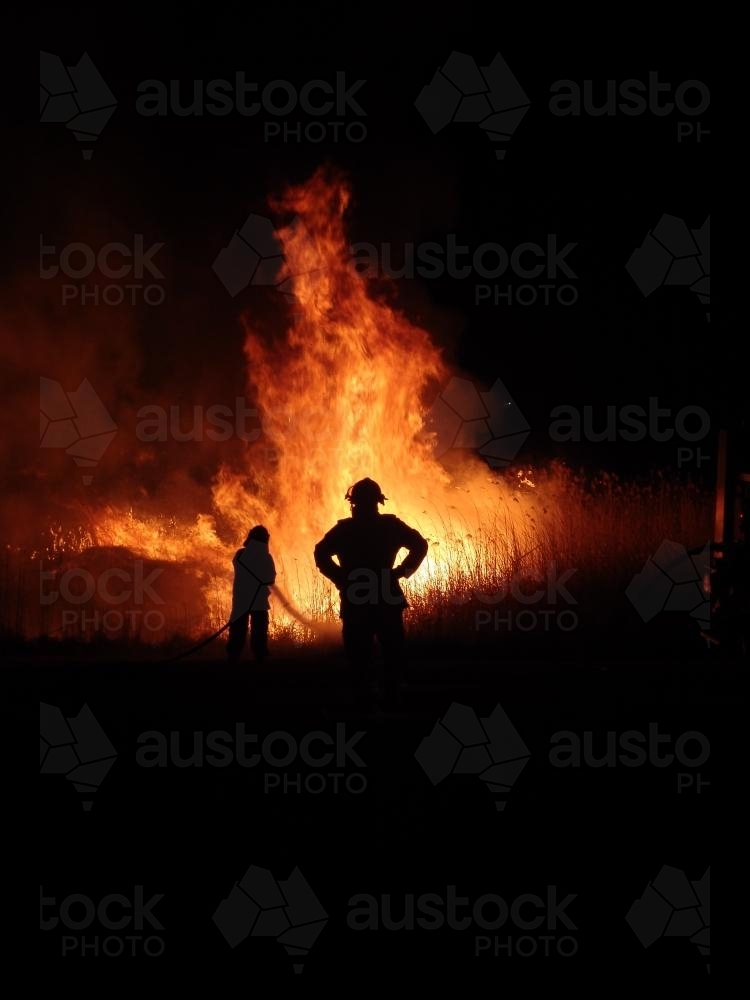 Firemen fighting a grass fire at night silhouetted against the fire - Australian Stock Image