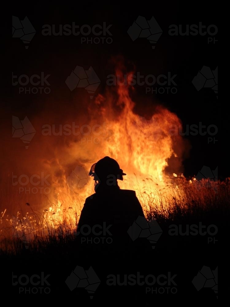 Firemen fighting a grass fire at night silhouetted against the flames - Australian Stock Image