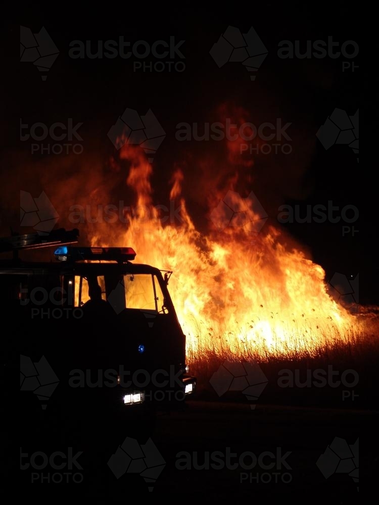 Firetruck silhouetted against a grass fire at night - Australian Stock Image