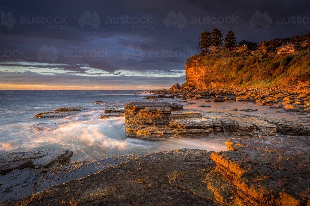 First light at Avalon beach, rich golden orange tones of light striking the cliff faces and rocks - Australian Stock Image