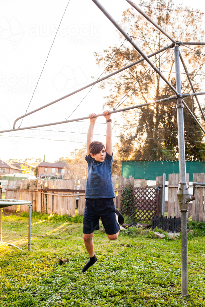 First Nations Australian boy swinging on hills hoist rotary clothesline in Aussie backyard - Australian Stock Image