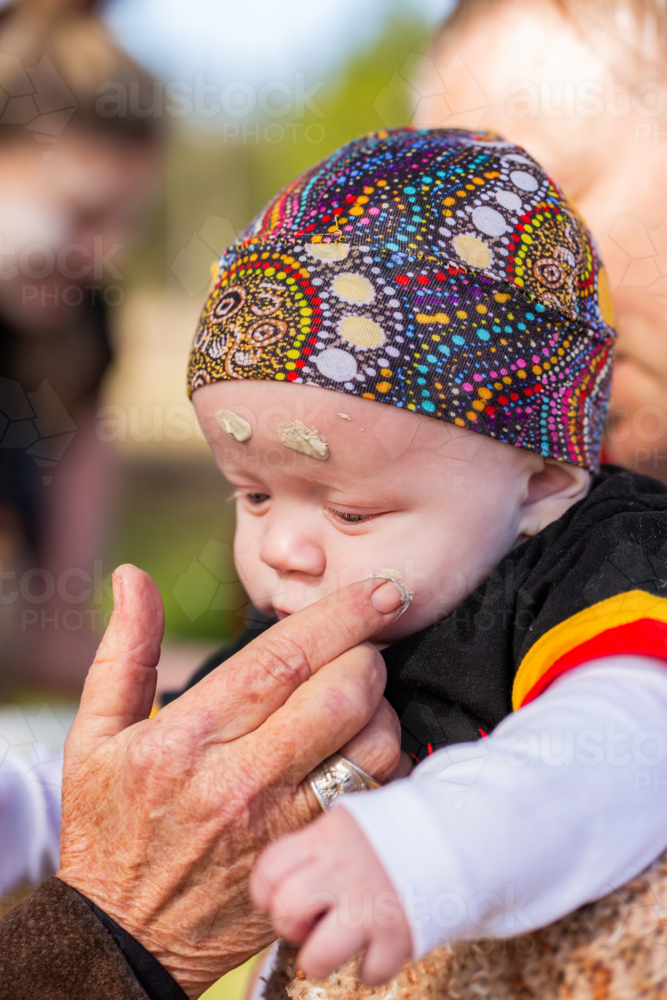 First nations Australian elder welcoming baby  to country putting ochre on face - Australian Stock Image