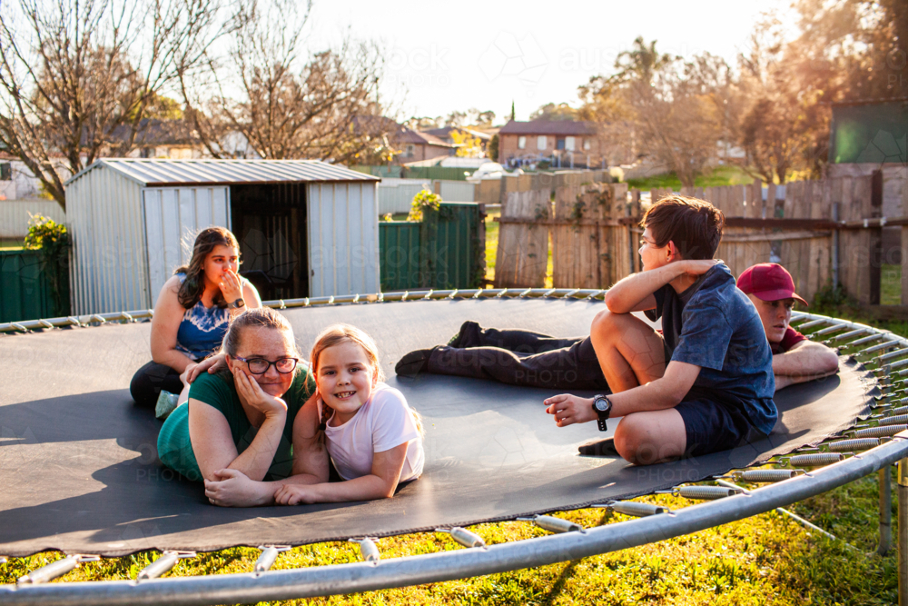 First Nations Australian family lying on trampoline together in backyard - Australian Stock Image