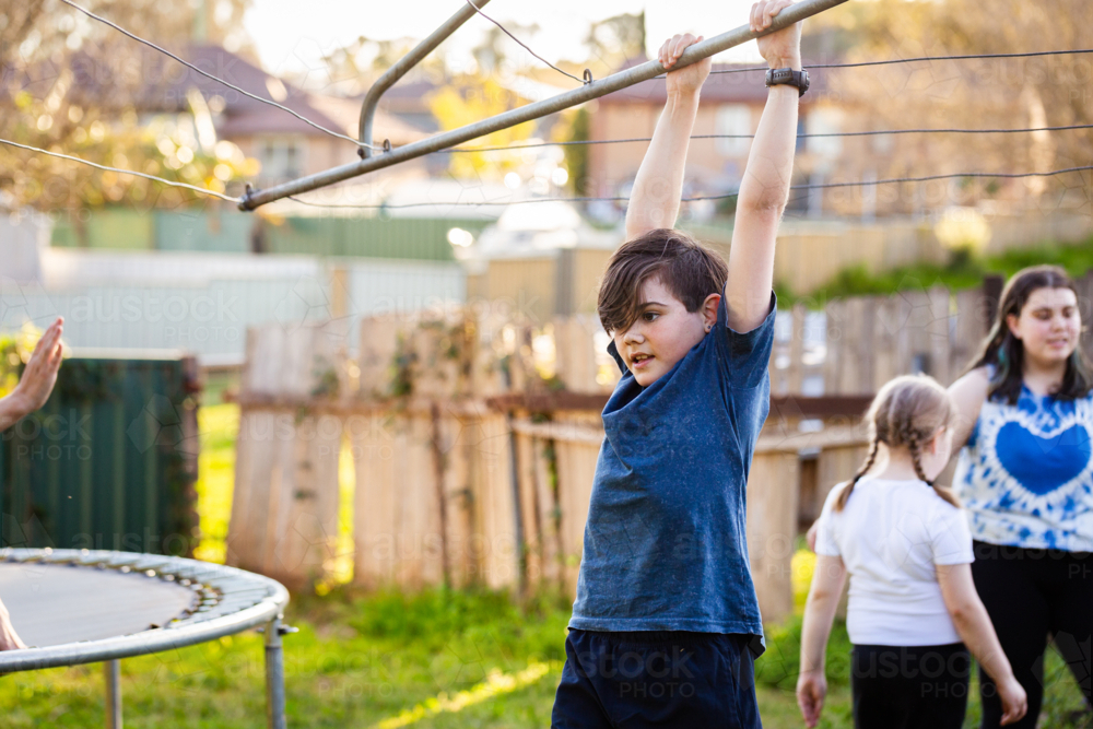 First Nations Australian kid swinging on hills hoist rotary clothesline in Aussie backyard - Australian Stock Image