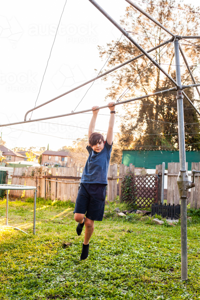 First Nations Australian kid swinging on hills hoist rotary clothesline in Aussie backyard - Australian Stock Image