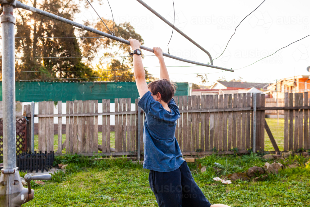 First Nations Australian kid swinging on hills hoist rotary clothesline in Aussie backyard - Australian Stock Image
