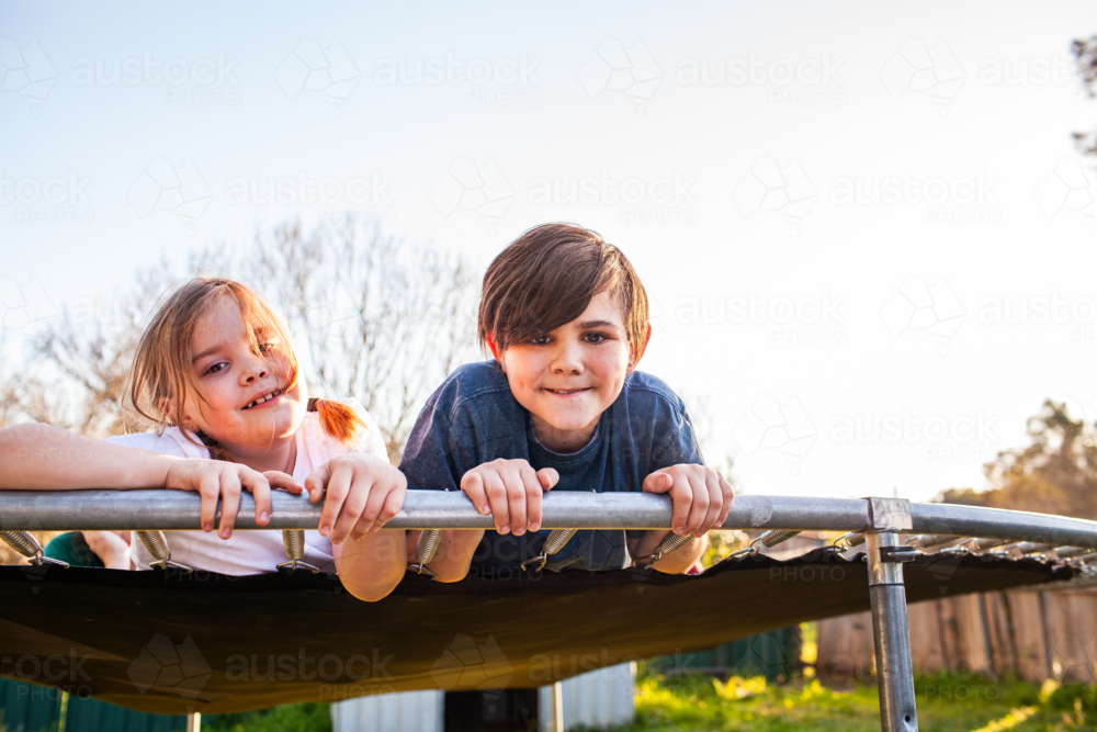 First Nations Australian kids sister and brother lying on trampoline together in Aussie backyard - Australian Stock Image