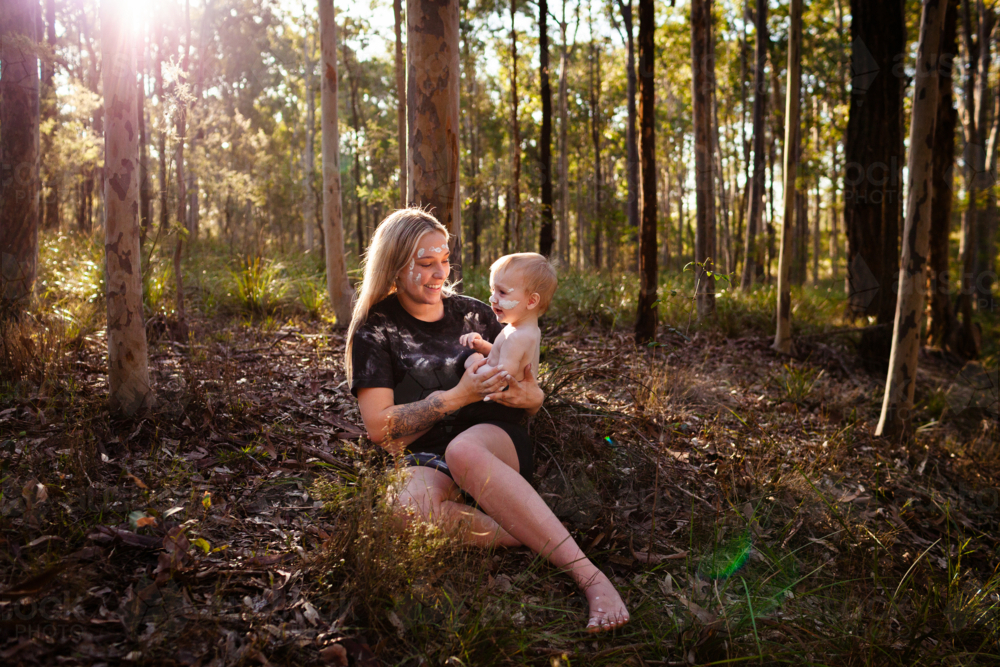 First Nations Australian mum with baby boy sitting enjoying National Park bushland together - Australian Stock Image