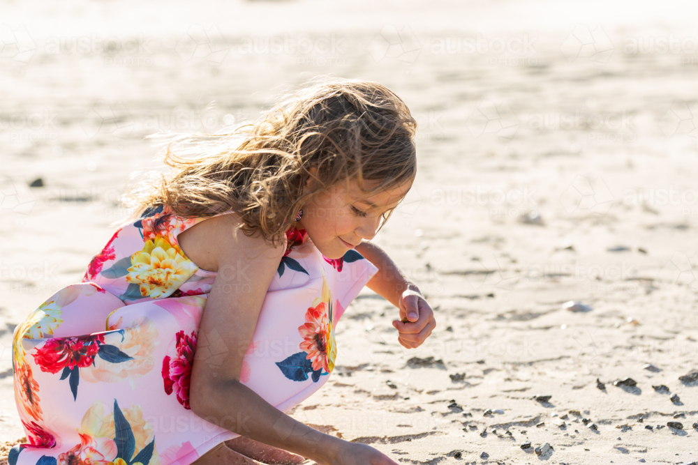 First Nations Australian Torres Strait Islander girl crouching in the sand on windy day at the beach - Australian Stock Image