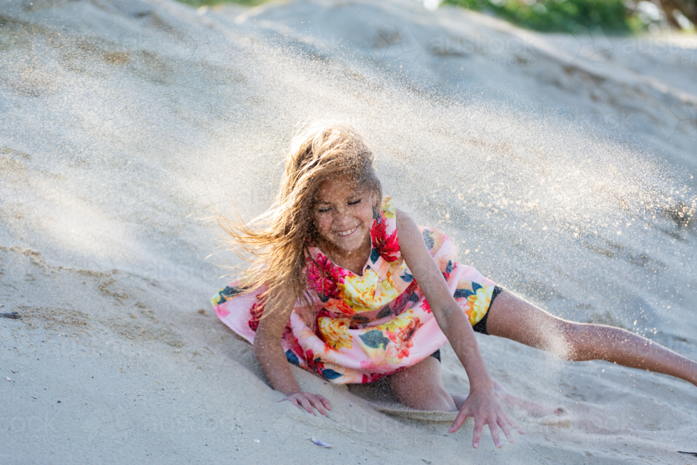 First Nations Australian Torres Strait Islander kid rolling down sand dune at the beach - Australian Stock Image