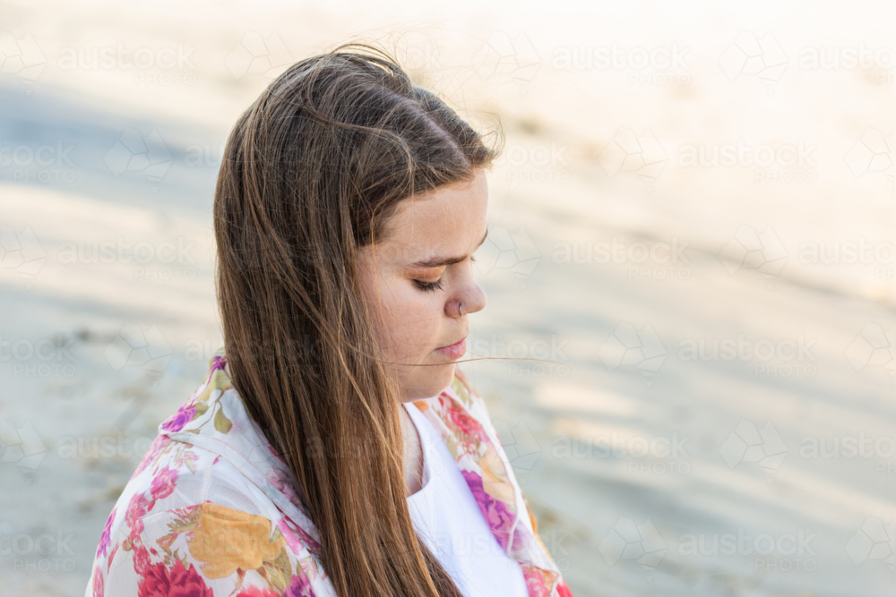 First Nations Australian Torres Strait Islander teen girl sitting on beach sand dune looking down - Australian Stock Image