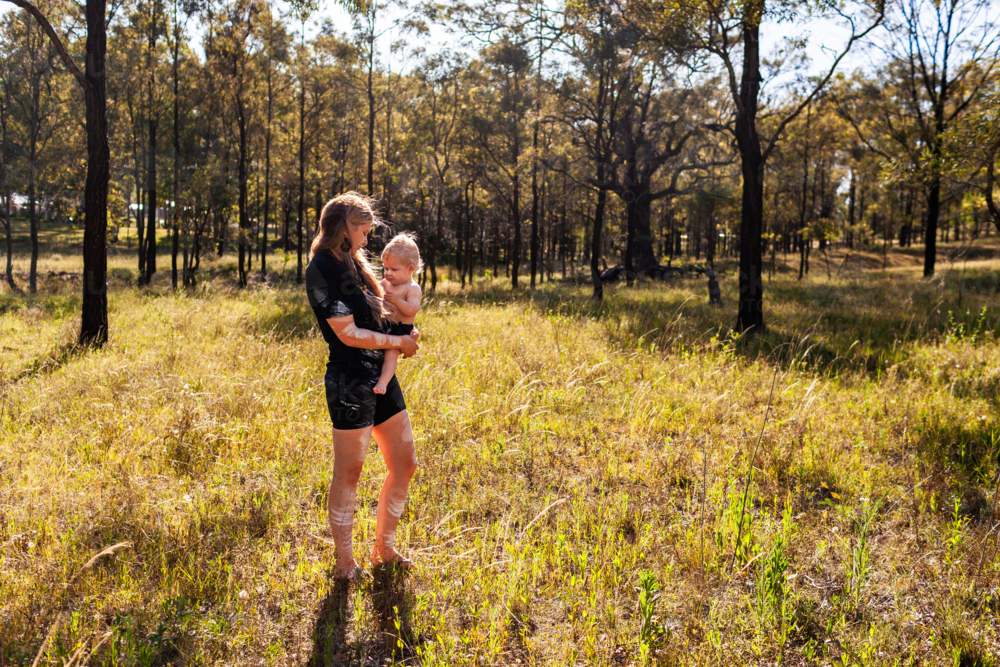 First nations Australian woman with baby boy walking in Australian paddock bushland - Australian Stock Image