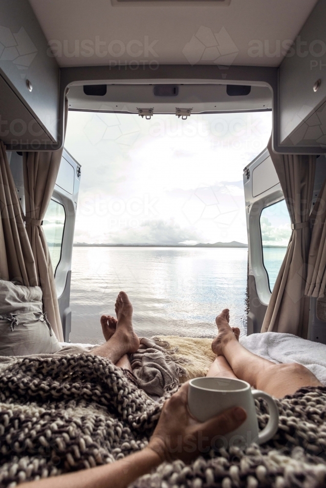 first person perspective of barefoot couple relaxing in a camping van with an ocean view - Australian Stock Image