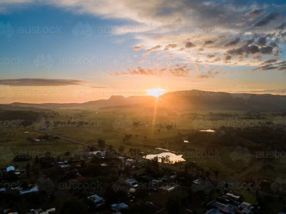 first rays of sunshine at sunrise in Broke peeking from hills in rural farmland - Australian Stock Image