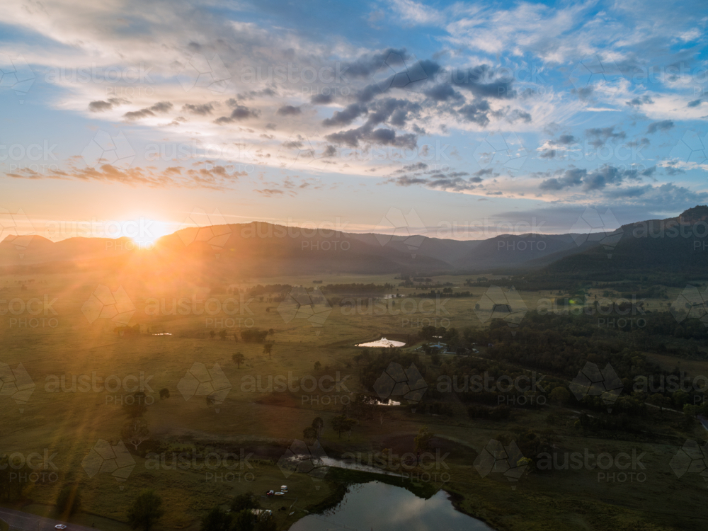 first rays of sunshine at sunrise in Broke peeking from hills in rural farmland reflecting in dams - Australian Stock Image