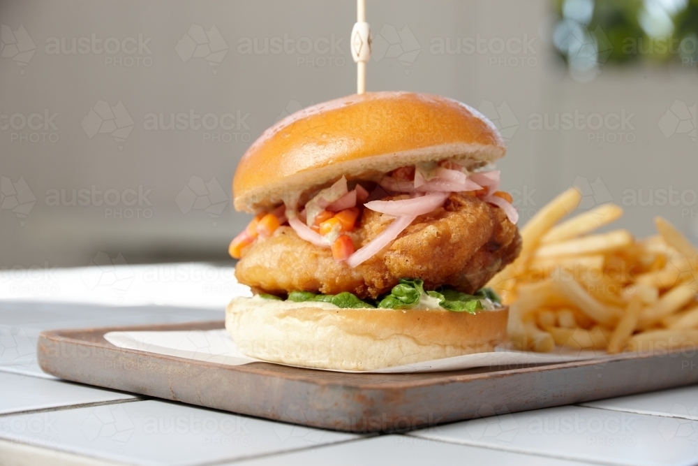 Fish burger on board with fries - Australian Stock Image