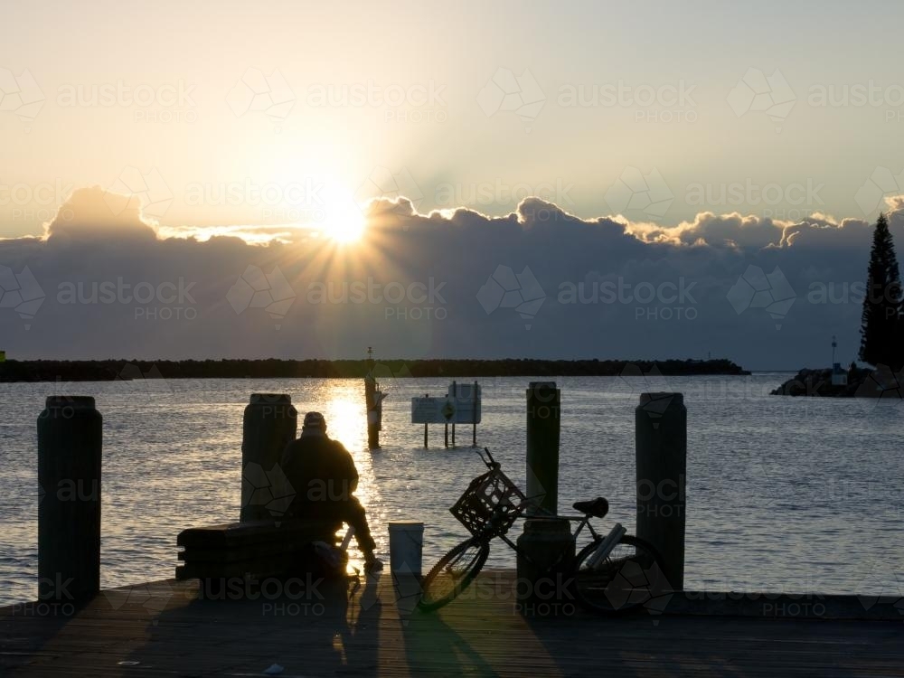 Fisherman and bike on a jetty facing the sunrise - Australian Stock Image