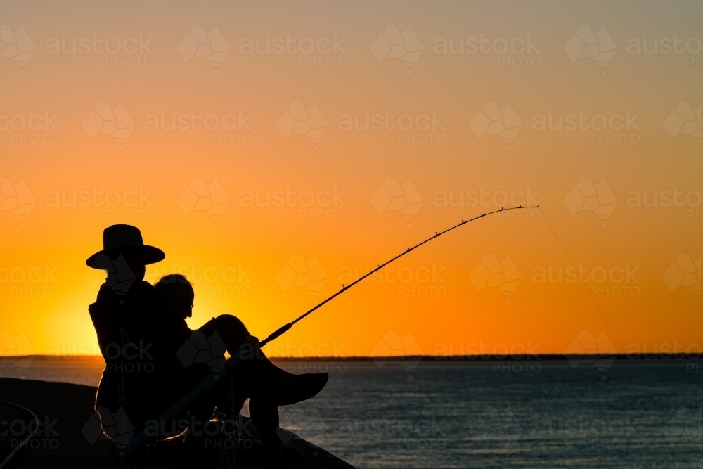 Fisherman and companion on a jetty silhouetted in the sunset - Australian Stock Image