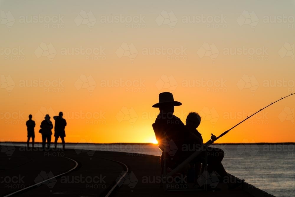 Fisherman and people silhouetted in sunset - Australian Stock Image