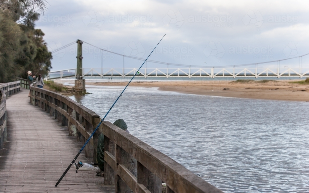 Fisherman at coastal river with bridge in background - Australian Stock Image