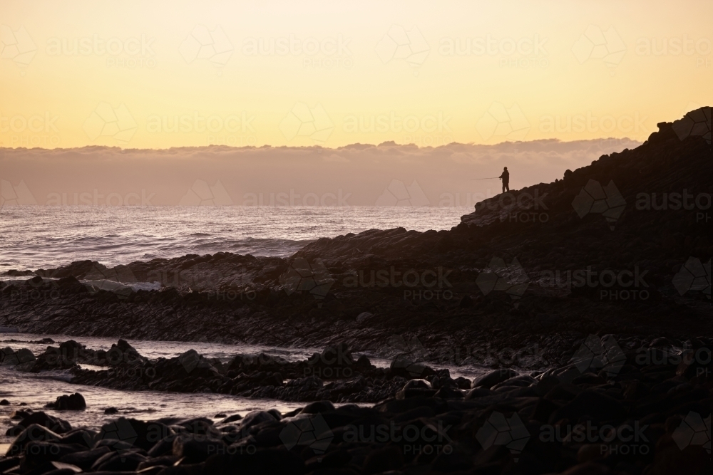 Fisherman fishing in coastal landscape on sunrise - Australian Stock Image