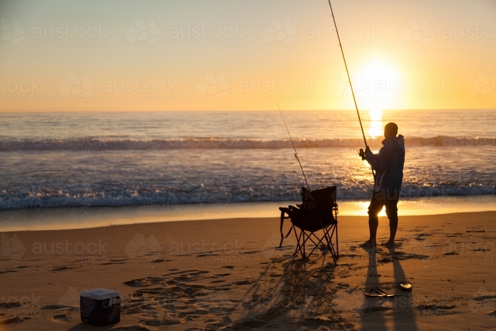 Fisherman fishing of beach at sunrise on clear morning - Australian Stock Image
