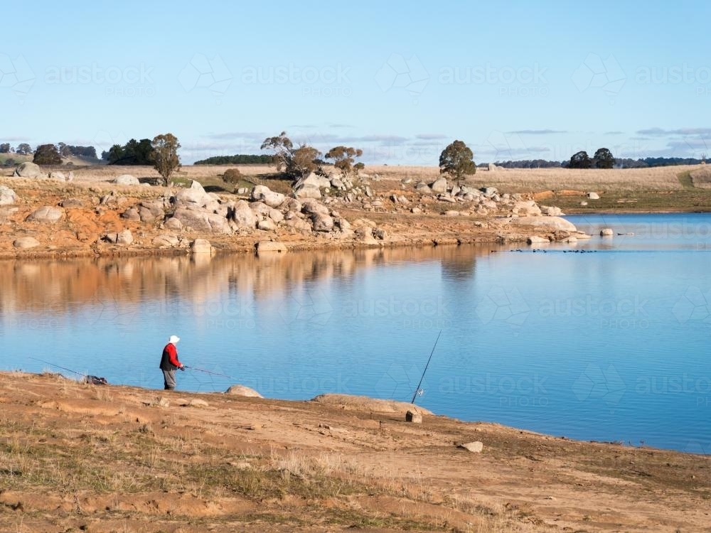 Fisherman fishing on the granite shores of a lake on a sunny day - Australian Stock Image