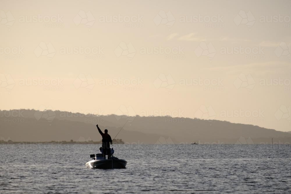 Fisherman in a Boat with Arm Raised Triumphantly - Australian Stock Image