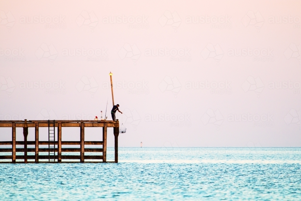 Fisherman lowering a crab pot from jetty in Wallaroo - Australian Stock Image