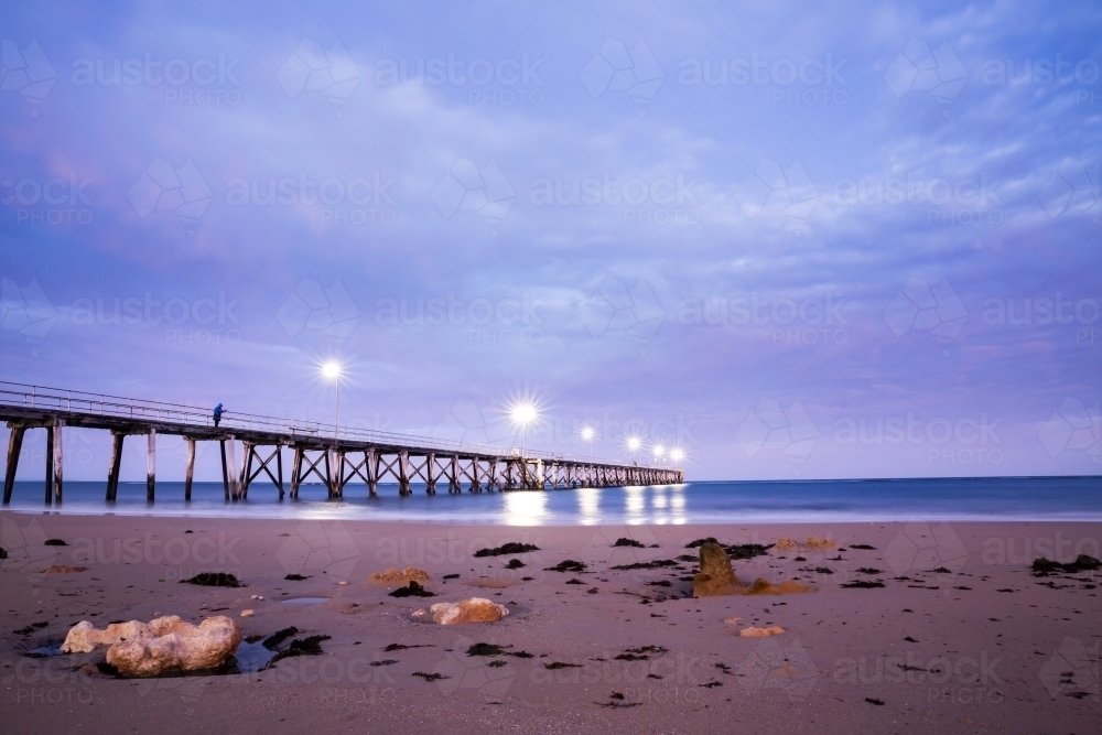 fisherman on jetty at dawn under cloudy sky - Australian Stock Image