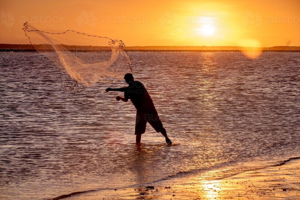 Fisherman throwing a cast net at sunset. - Australian Stock Image