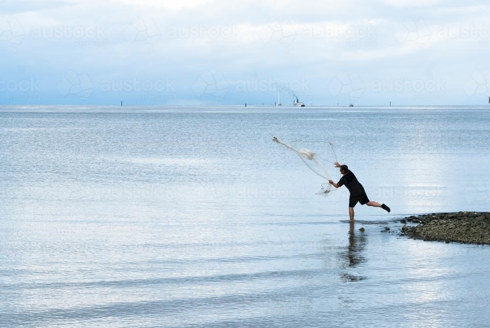 Fisherman throwing bait net on foreshore - Australian Stock Image