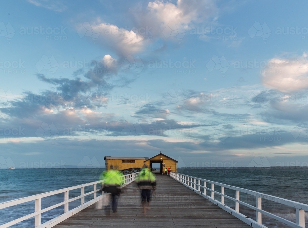 fisherman walking up a pier in late evening - Australian Stock Image