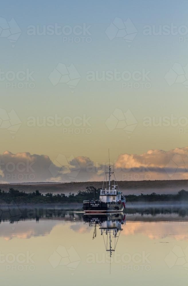 Fishing boat on calm waters with reflection - Australian Stock Image