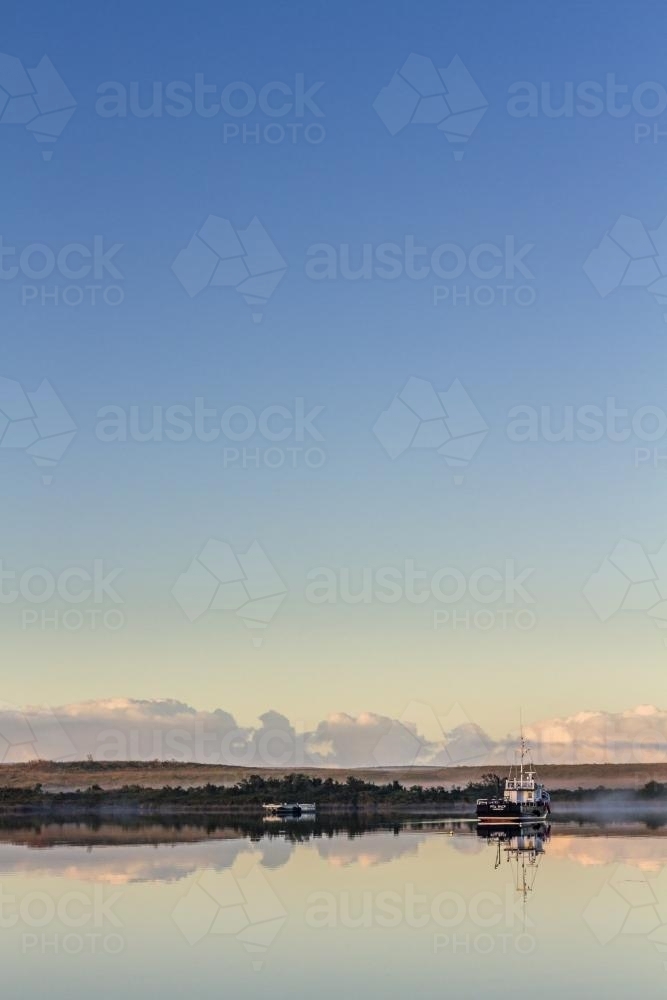 Fishing boat on calm waters with reflection - Australian Stock Image