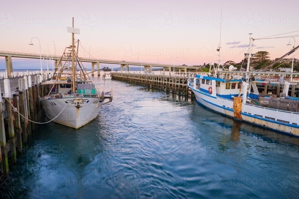 Image of Fishing boats docked at a jetty at twilight - Austockphoto
