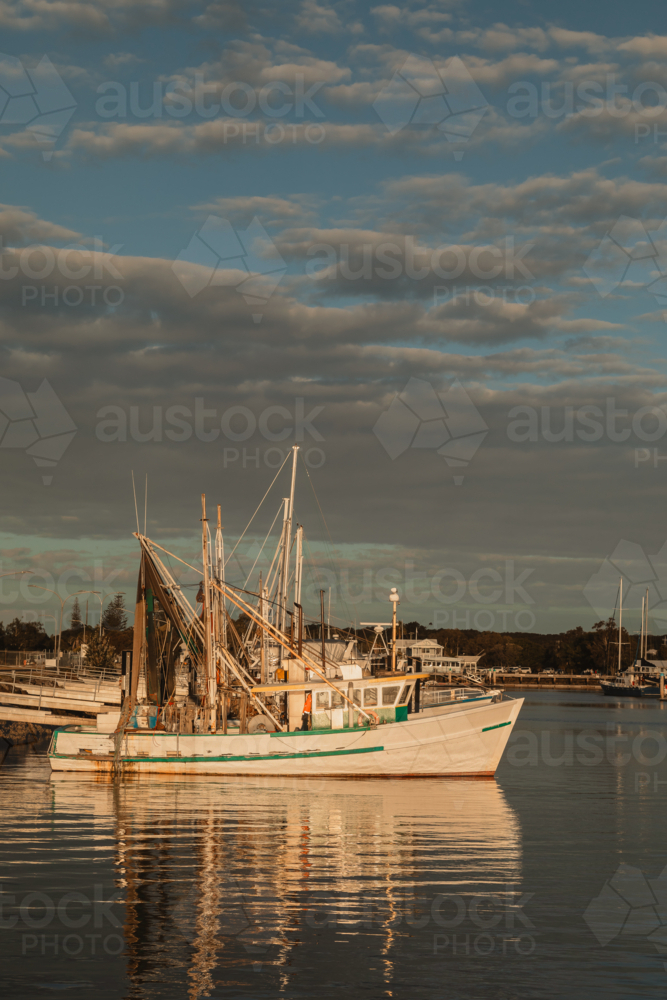Image of Fishing trawler docked in a calm harbor reflecting golden hour ...
